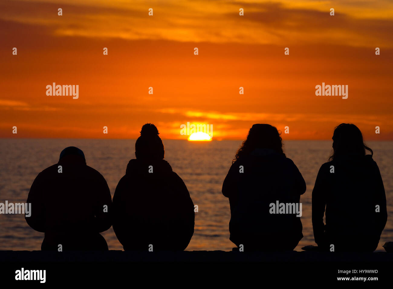 Aberystwyth Wales, UK. 2nd Apr, 2017. UK Weather: Four young people sitting in silhouette watching the setting sun over Cardigan Bay Aberystwyth Wales, at the end of a day of glorious warm weather and unbroken blue skies photo Credit: Keith Morris/Alamy Live News Stock Photo