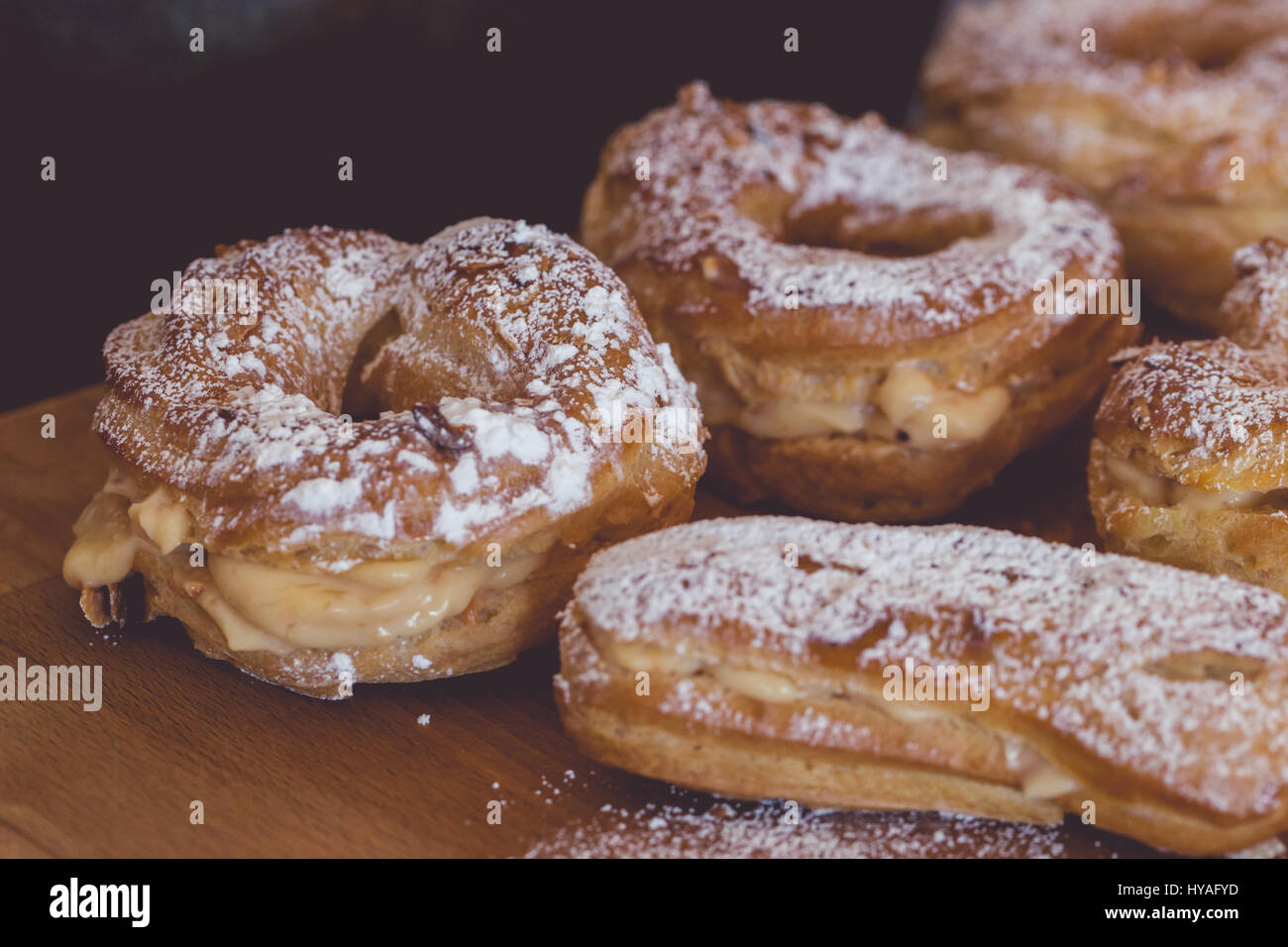 Variety of freshly baked profiteroles and eclairs filled in with vanilla cream and covered with sugar powder on rustic wooden board, close up Stock Photo