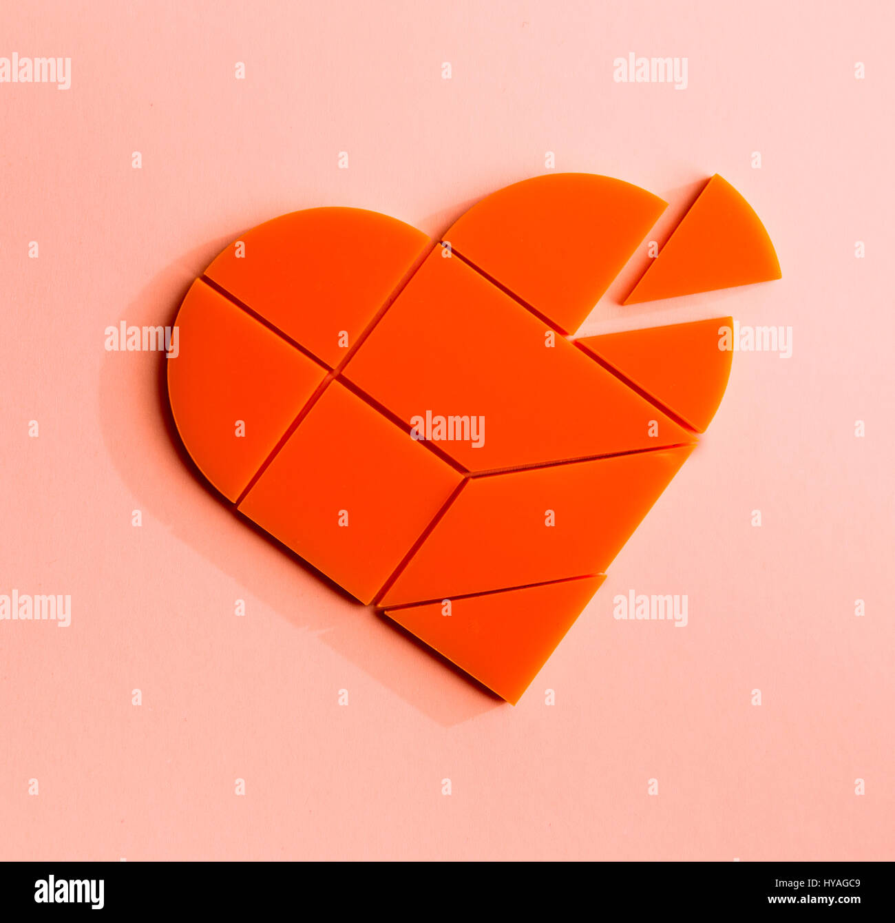 Plastic puzzle in the form of heart with disconnected piece on a pink background Stock Photo