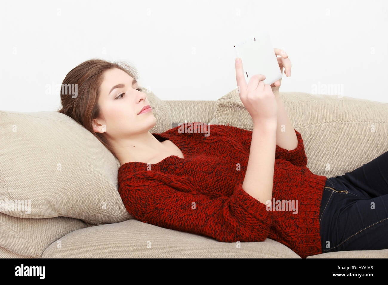 Young beautiful cheerful red-haired girl in a blue jeans jacket sitting on the couch at home and talking on a cell phone. Stock Photo