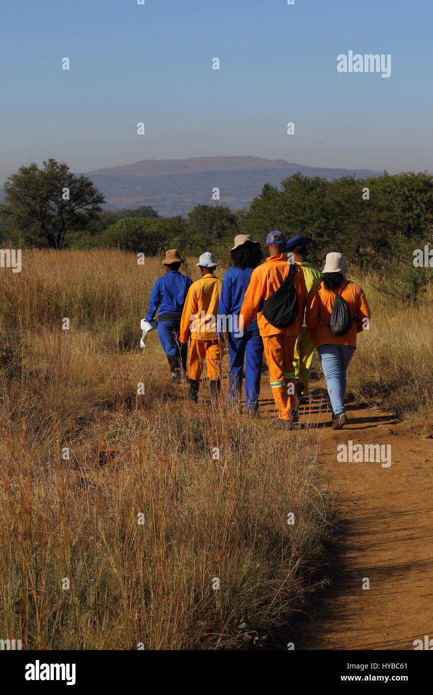 Black laborers in orange and blue overalls walk to work through the