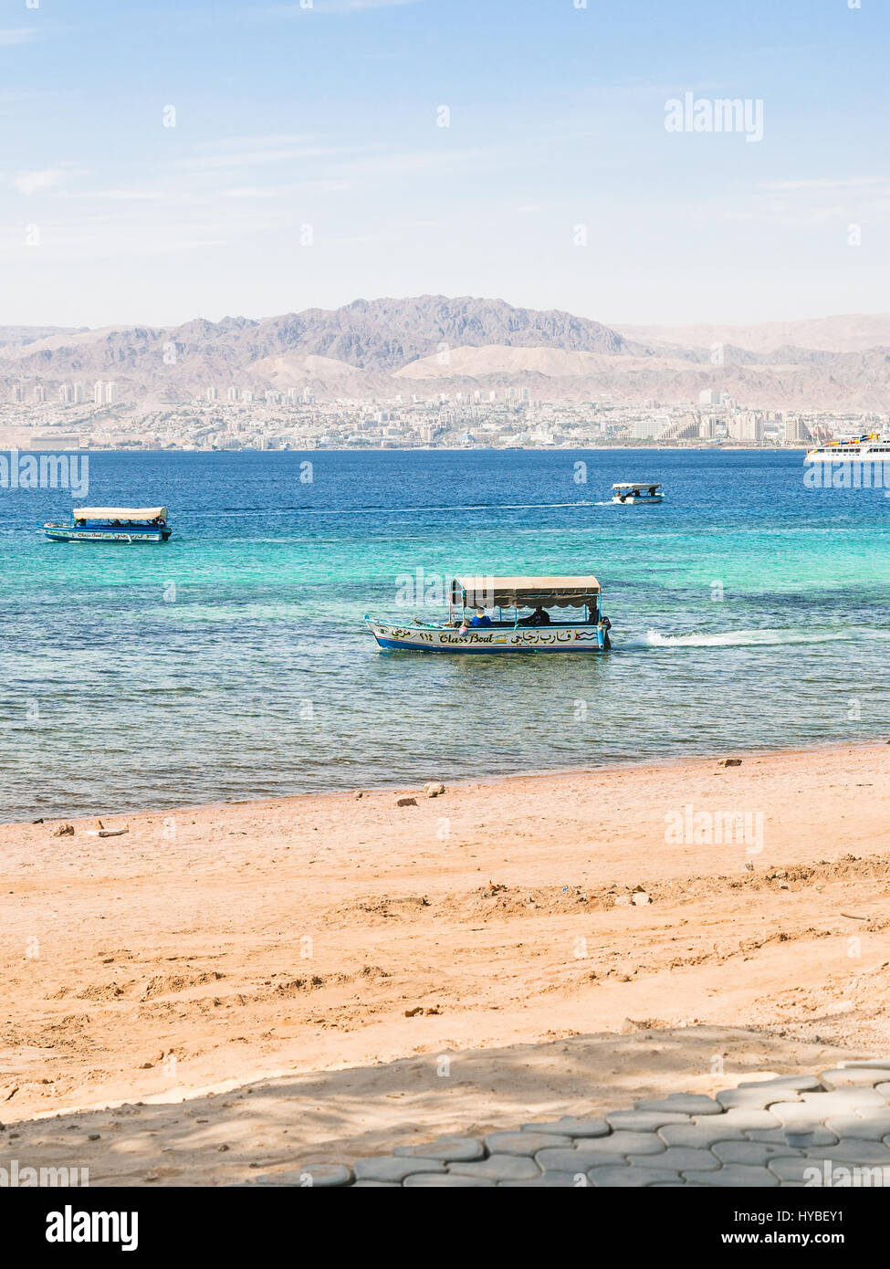 AQABA, JORDAN - FEBRUARY 23, 2012: boats near beach of Aqaba and view of Eilat city in background in winter. Jordan country has only one exit to sea i Stock Photo
