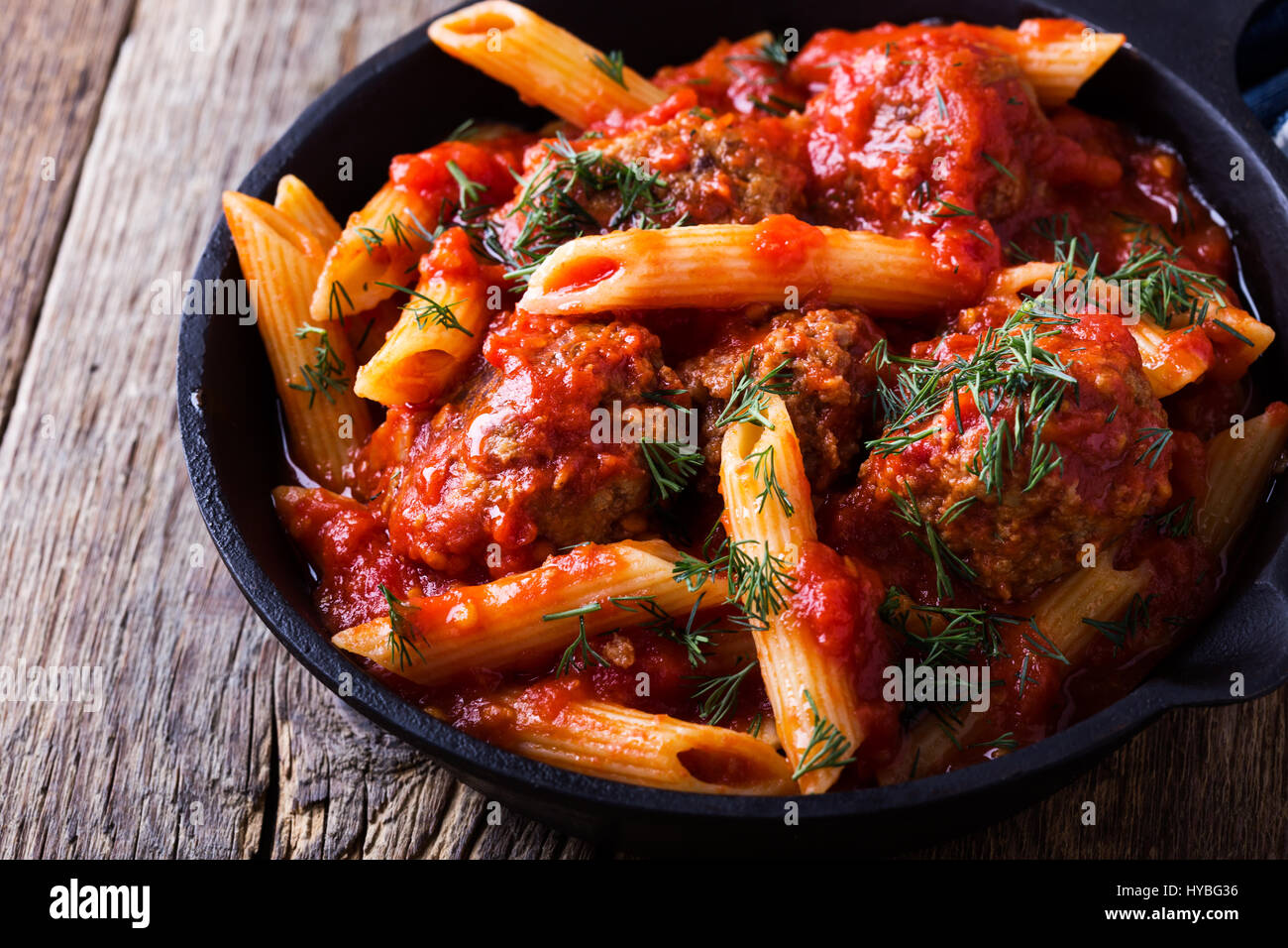 Meatball penne pasta with spicy tomato sauce and dill in cast iron pan ...