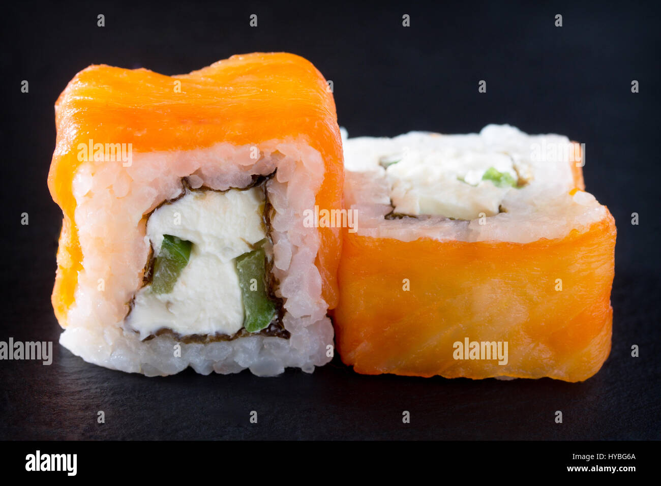 Roll isolate on a black slate board - tobiko green roe, perch Izumidai, spicy sauce, cucumber, nori, rice. Stock Photo