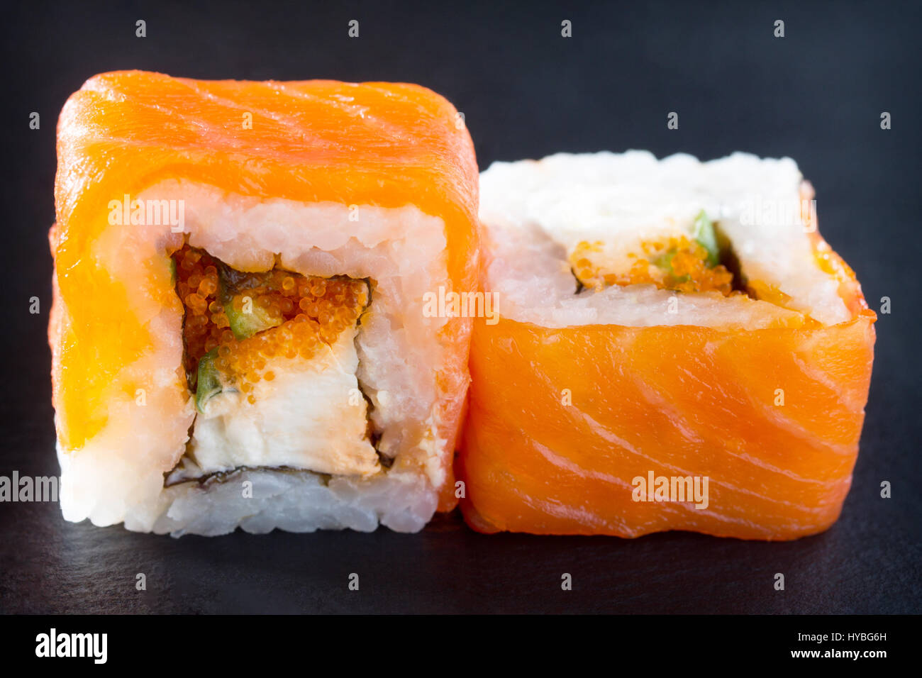 Roll isolate on a black slate board - tobiko green roe, perch Izumidai, spicy sauce, cucumber, nori, rice. Stock Photo