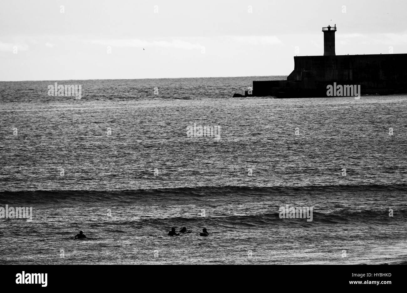 Some surfers at Matosinhos beach with the lighthouse as a scenario. Stock Photo