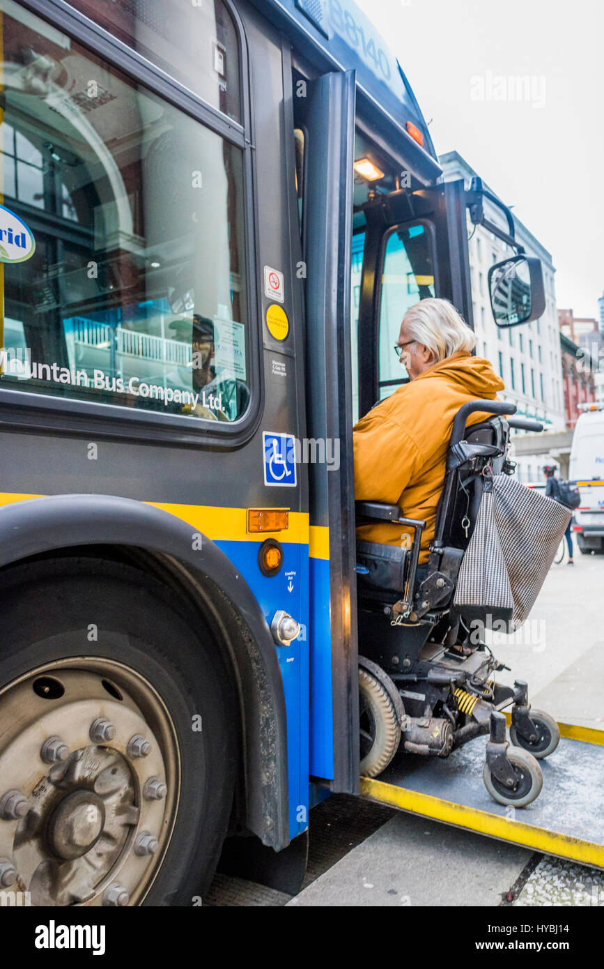 Man in wheelchair boards accessible bus via ramp, Vancouver, British Columbia, Canada. Stock Photo