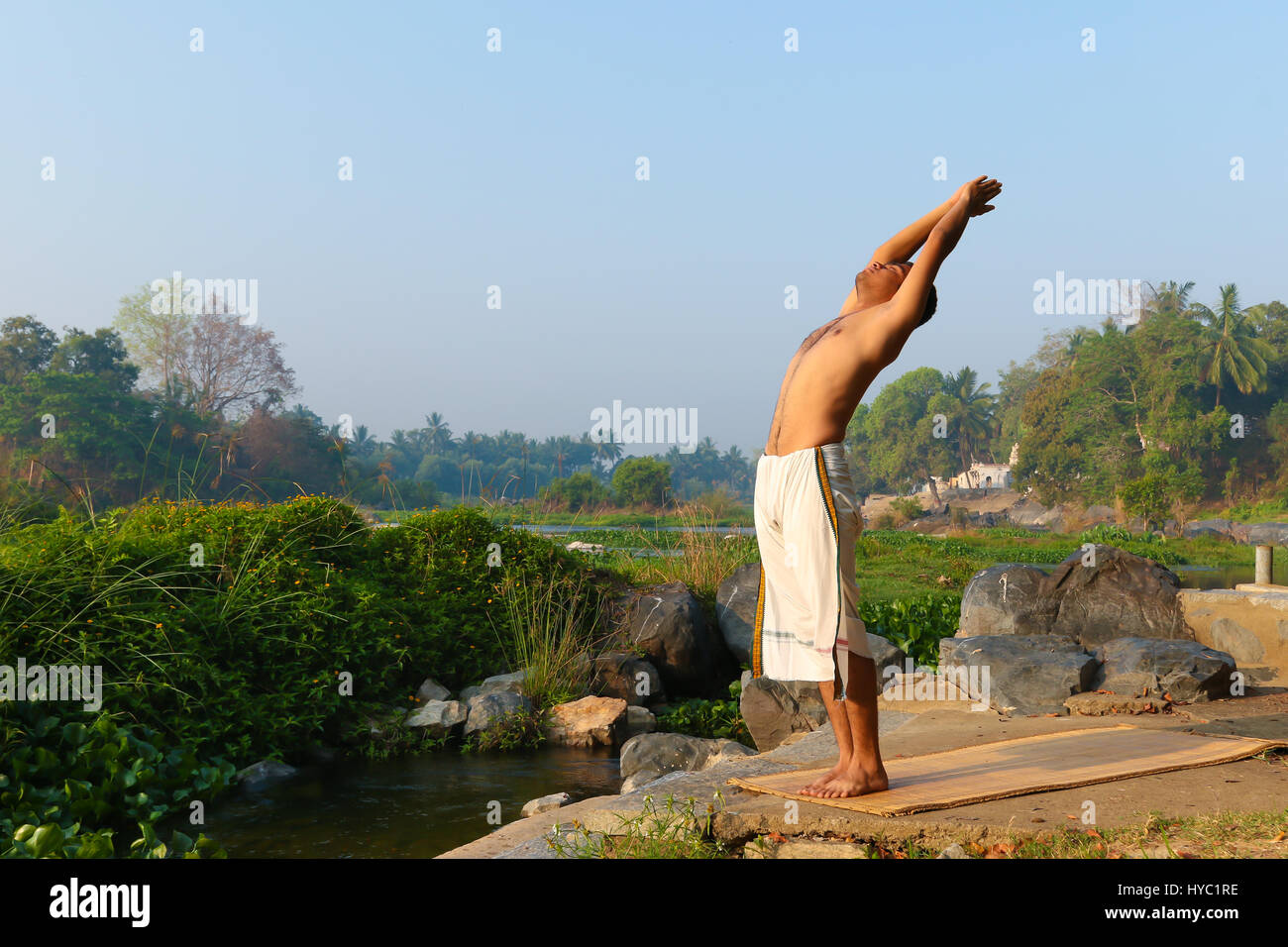Indian man practicing yoga next to a river  in South India. Stock Photo
