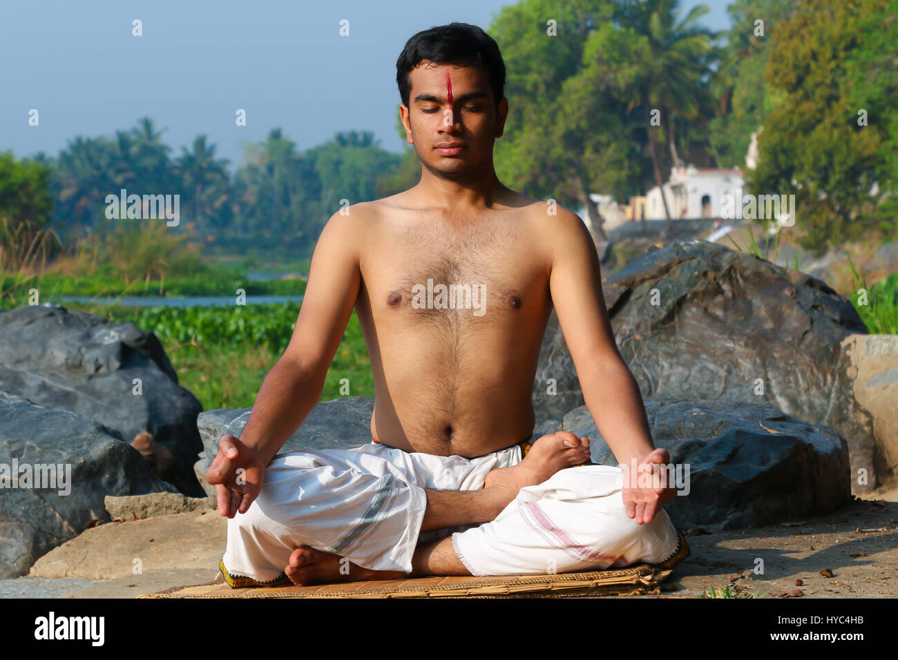Indian man practicing yoga meditation next to a river  in South India. Stock Photo