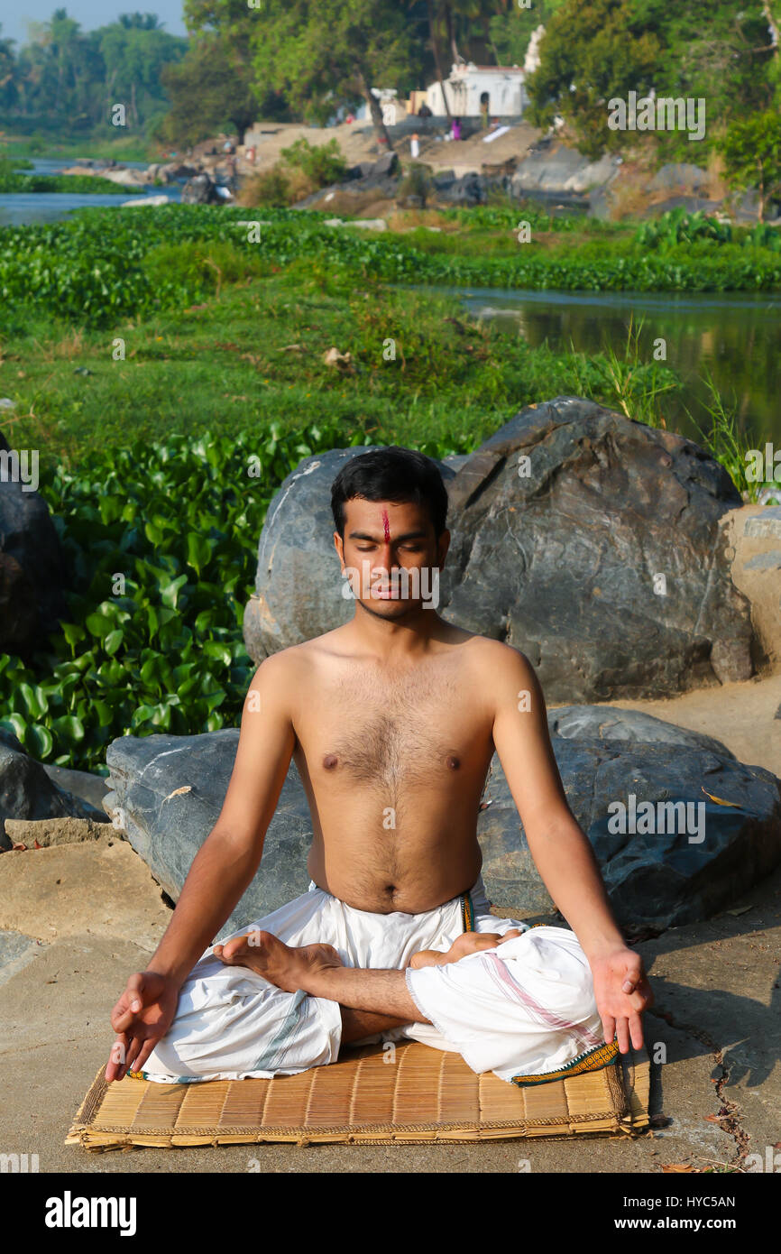 Indian man practicing yoga next to a river  in South India. Stock Photo