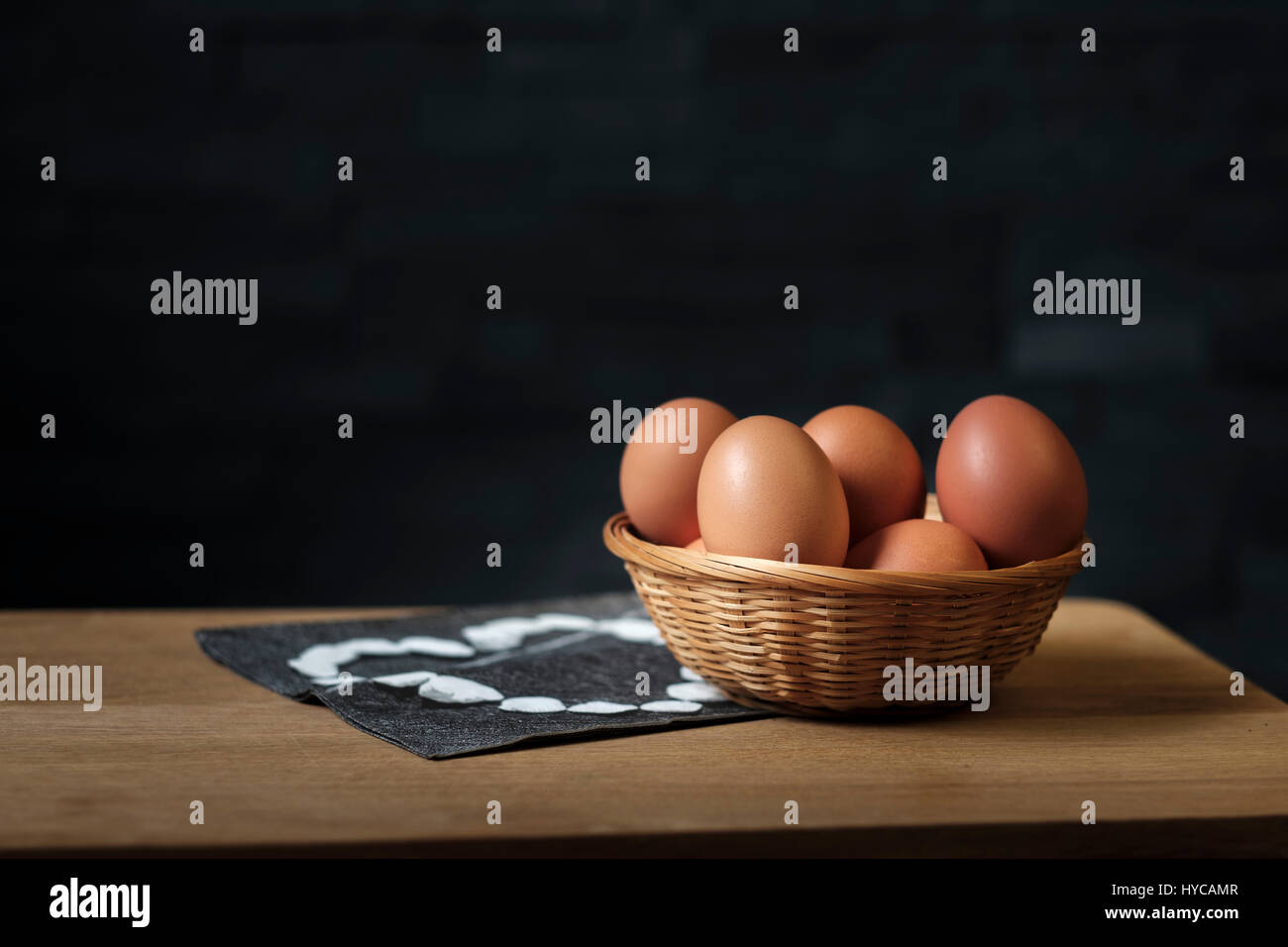 brown eggs in a wicker basket on a wooden board set against a black background Stock Photo