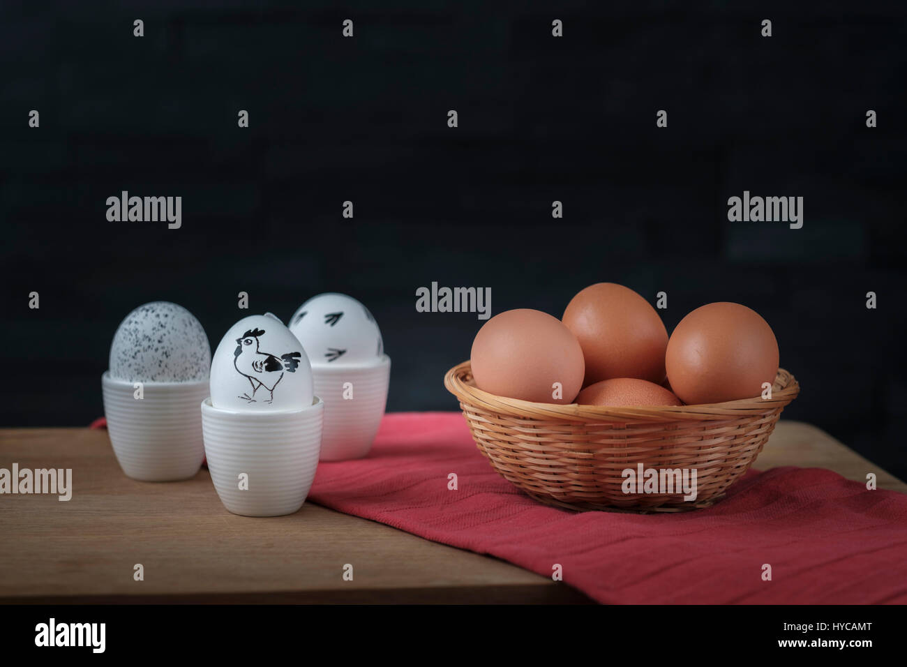 White easter eggs in an egg cup and brown eggs in a wicker basket on a red towel and a wooden plank Stock Photo