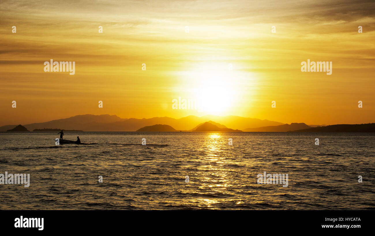 Silhouette of two fishermen on a small fishing boat with outboard motor ...