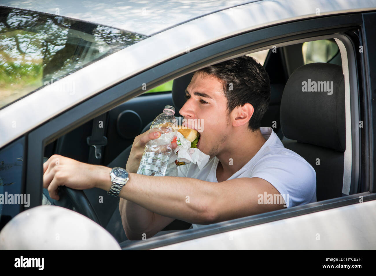 Young man driving his car while eating food Stock Photo
