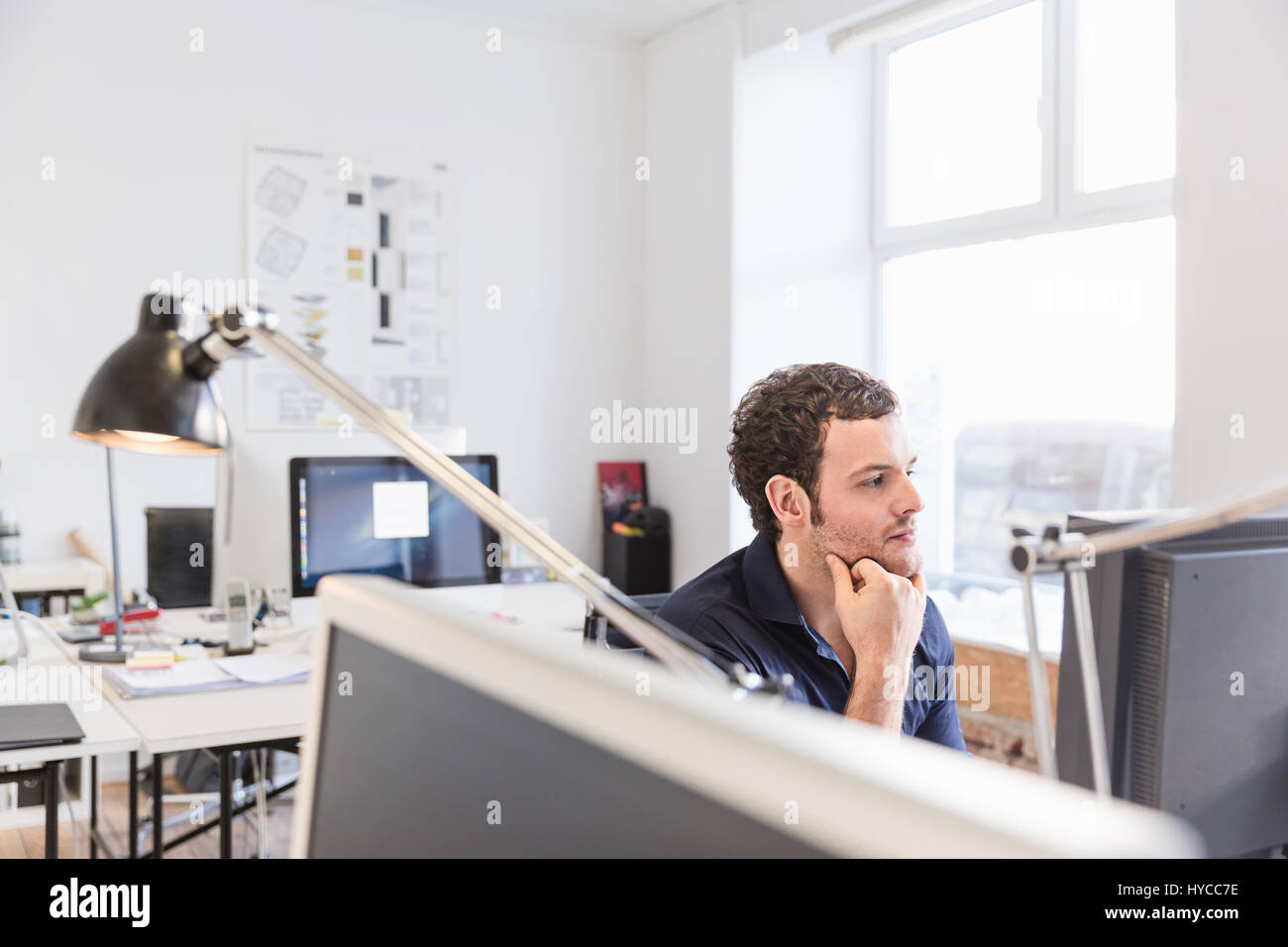 Mid adult man in office using computer hand on chin Stock Photo