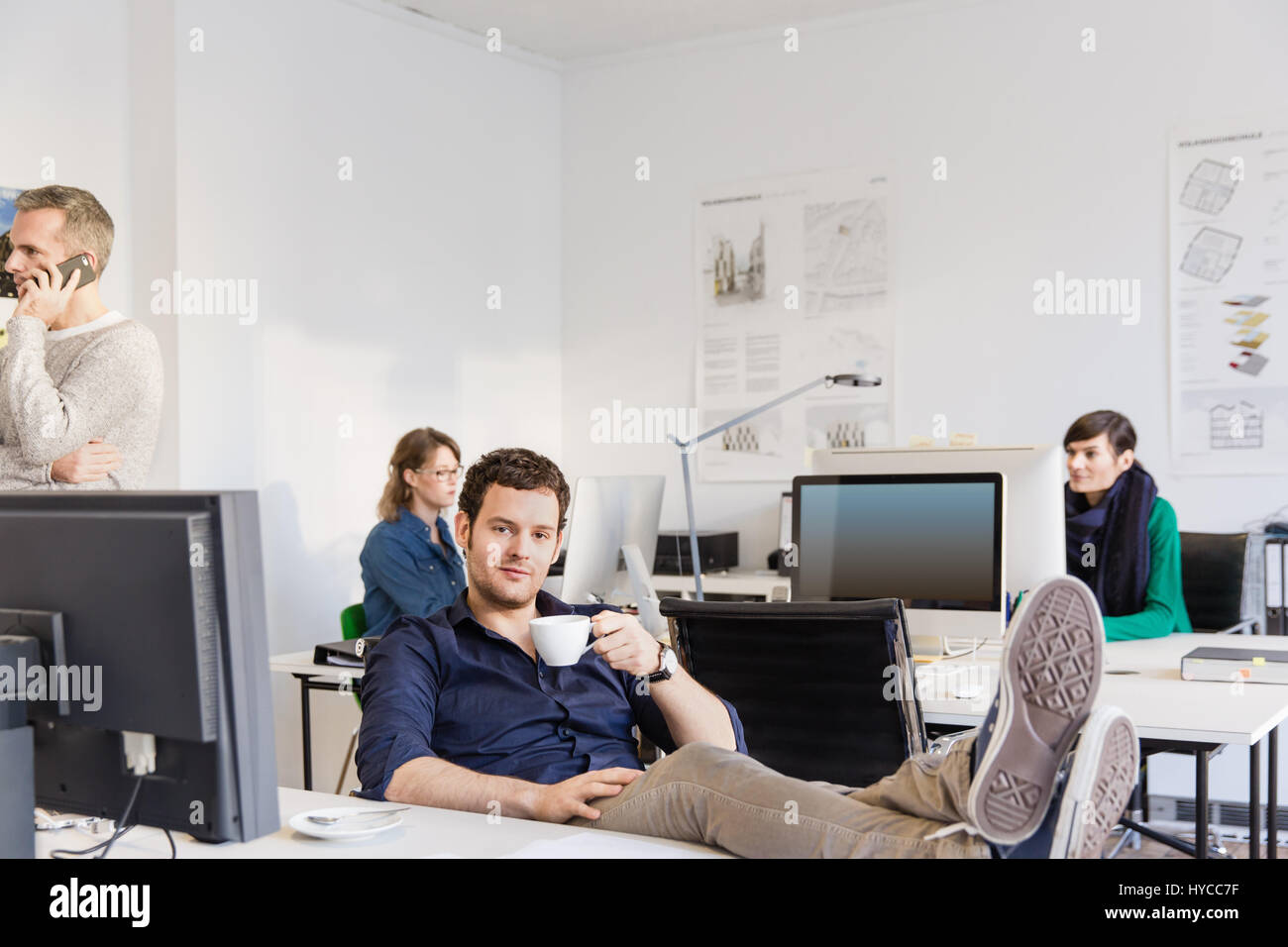 Mid adult man in office, feet on desk holding teacup looking at camera Stock Photo