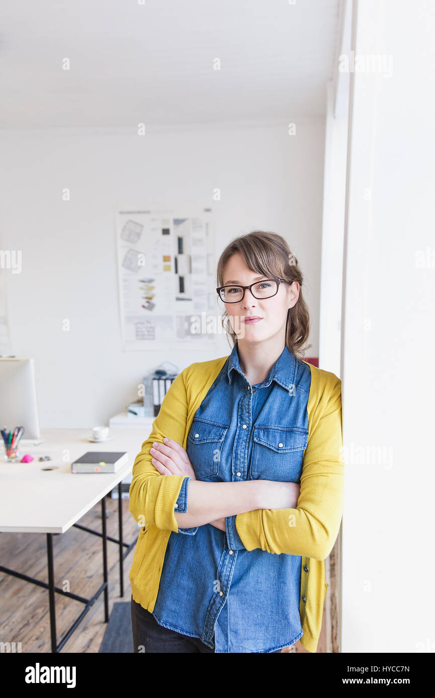Young woman leaning against wall in office arms crossed looking at camera Stock Photo
