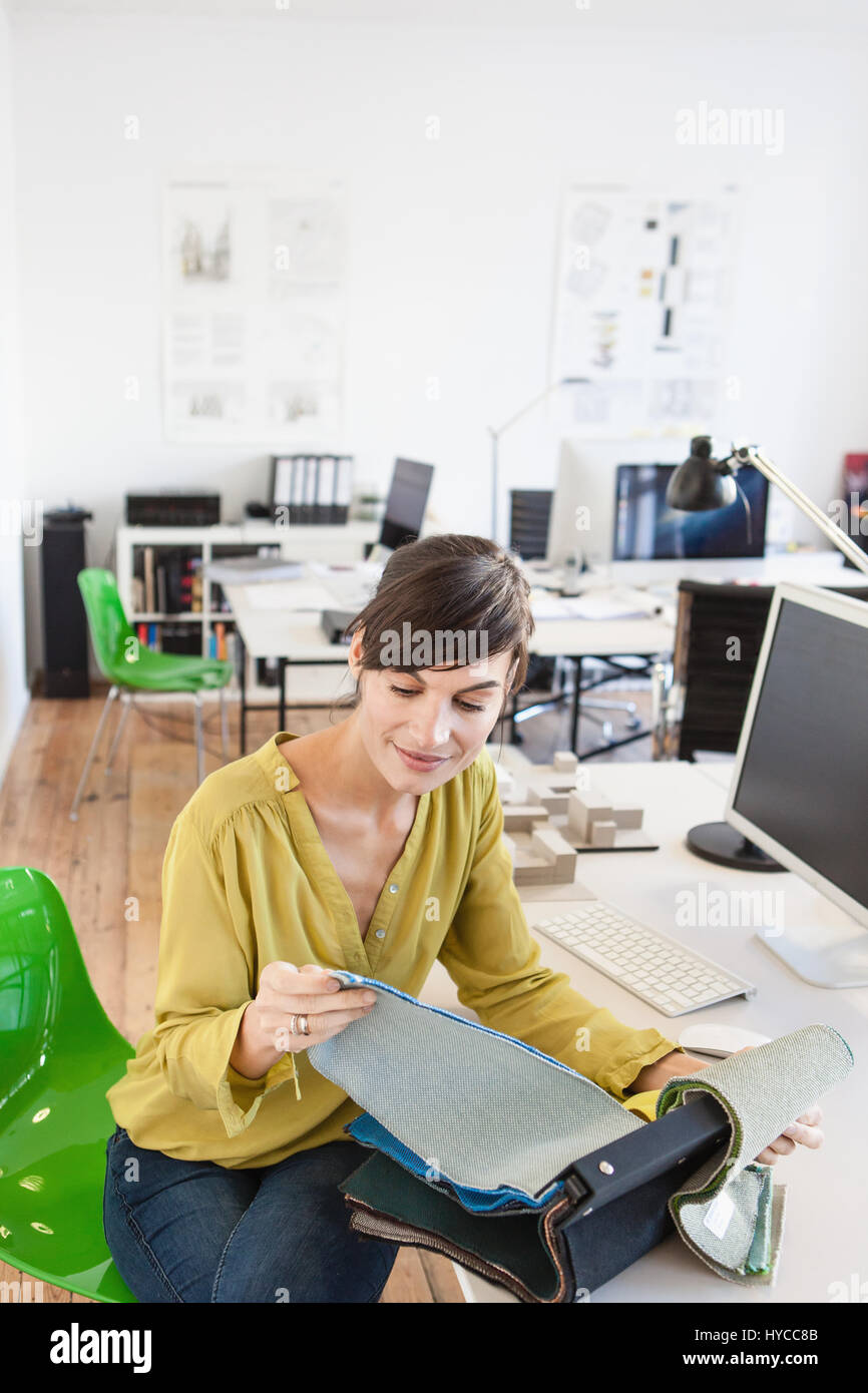 Mature woman in office sitting at desk looking through fabric swatches Stock Photo