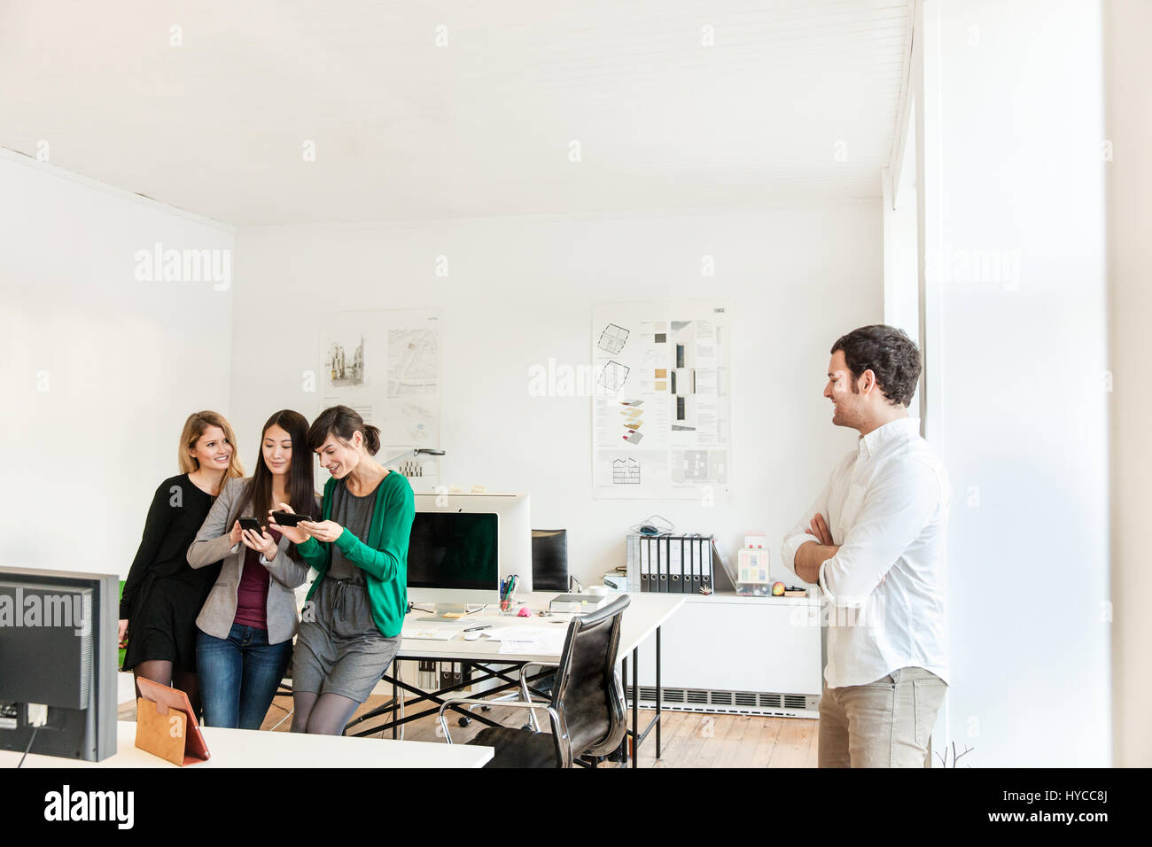 Mid adult man in office looking at colleagues using smartphones smiling Stock Photo