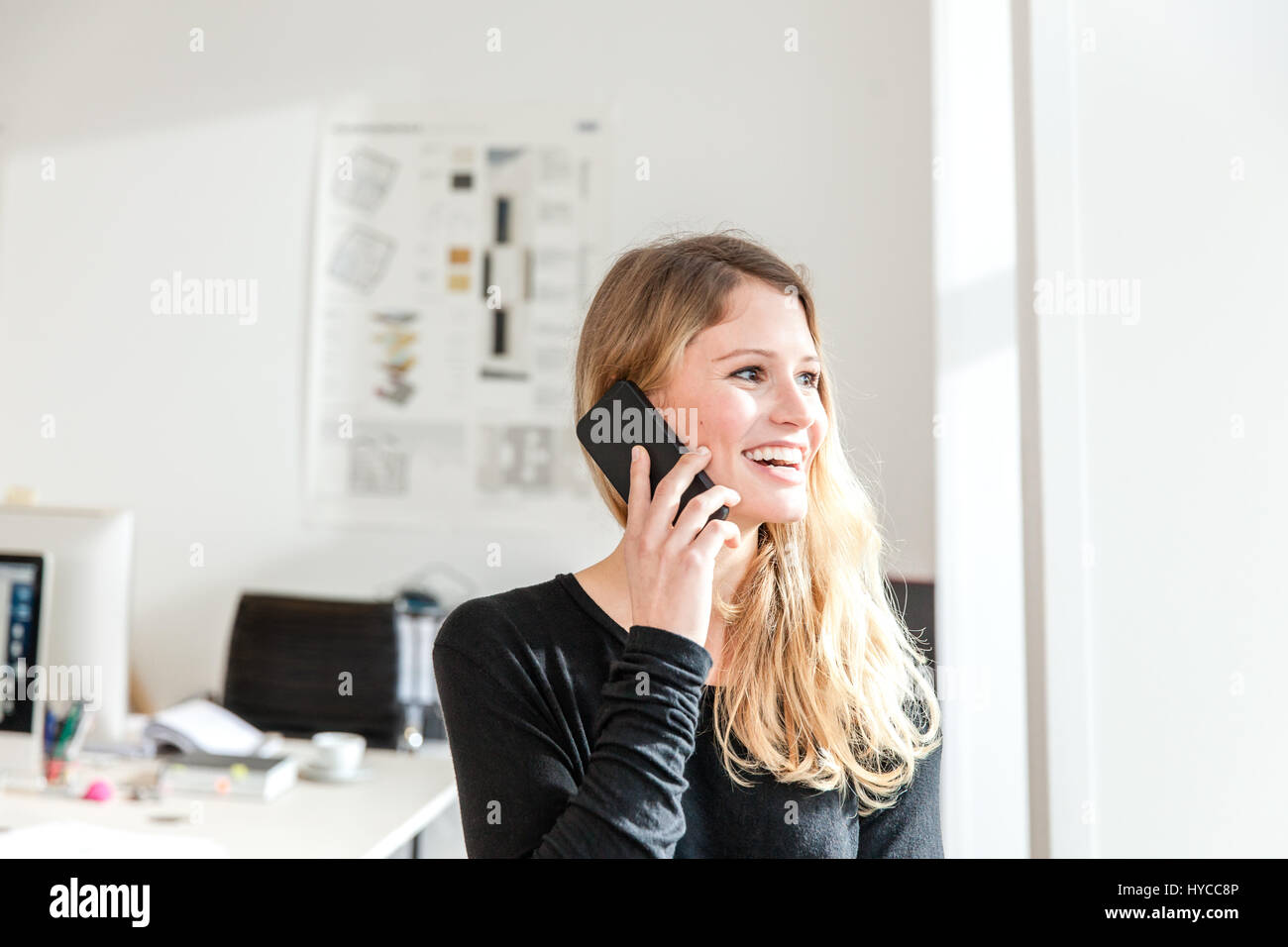 Young woman in office using smartphone to make telephone call looking away smiling Stock Photo