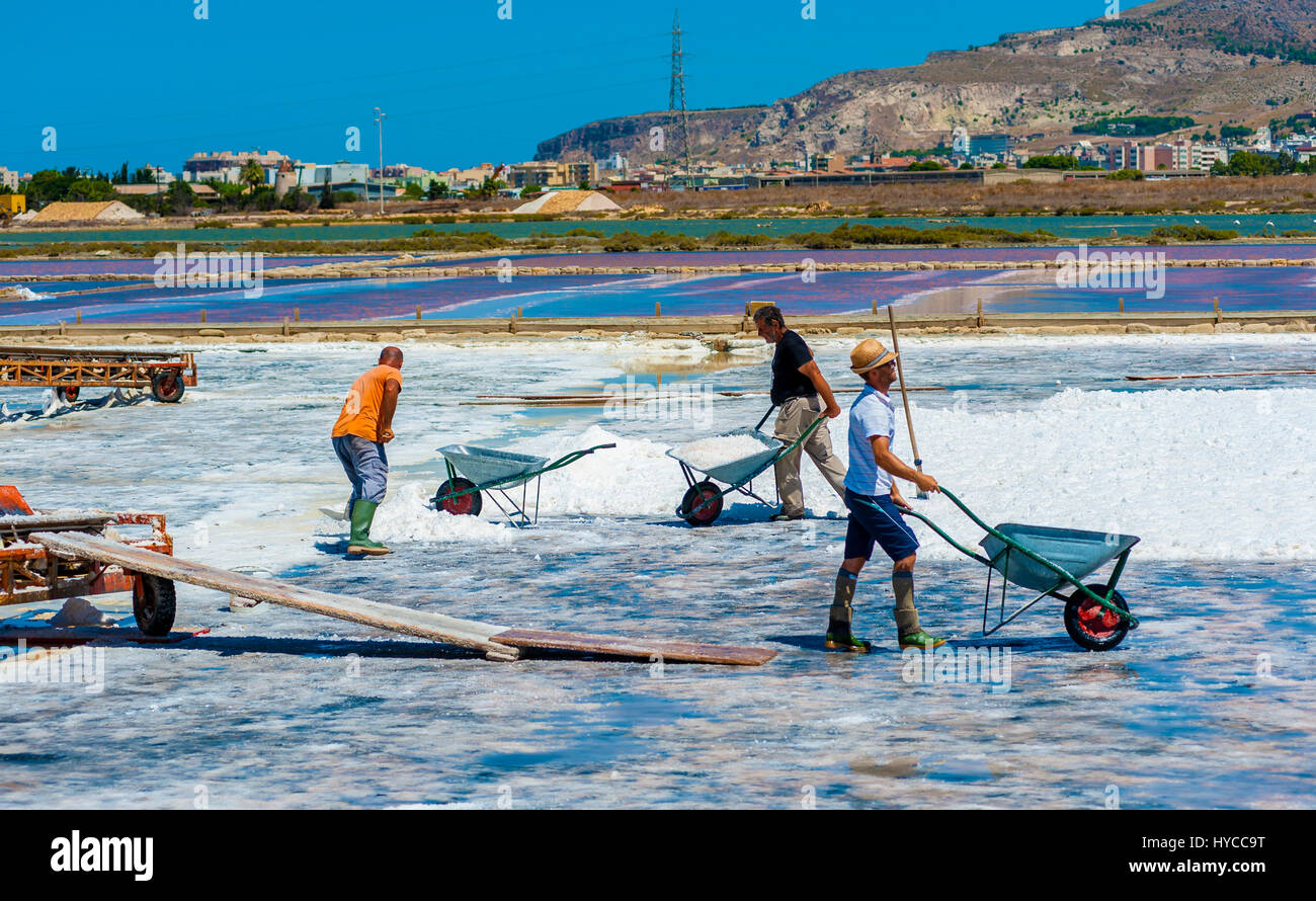 Trapani, August 13, 2016 - Italy: Workers shoveled the salt crystallizes out of the ground in salt farm , filled with natural salt from the sea. Stock Photo
