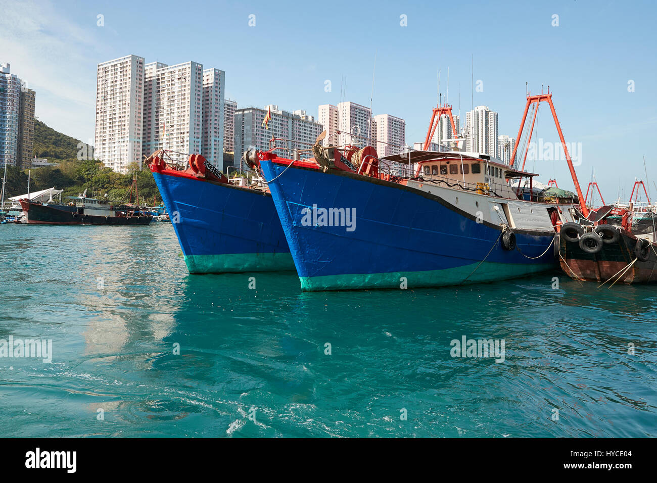 Brightly Painted Commercial Fishing Boats Moored In Aberdeen Channel, High Rise Apartment Buildings On Ap Lei Chau Island Behind. Stock Photo