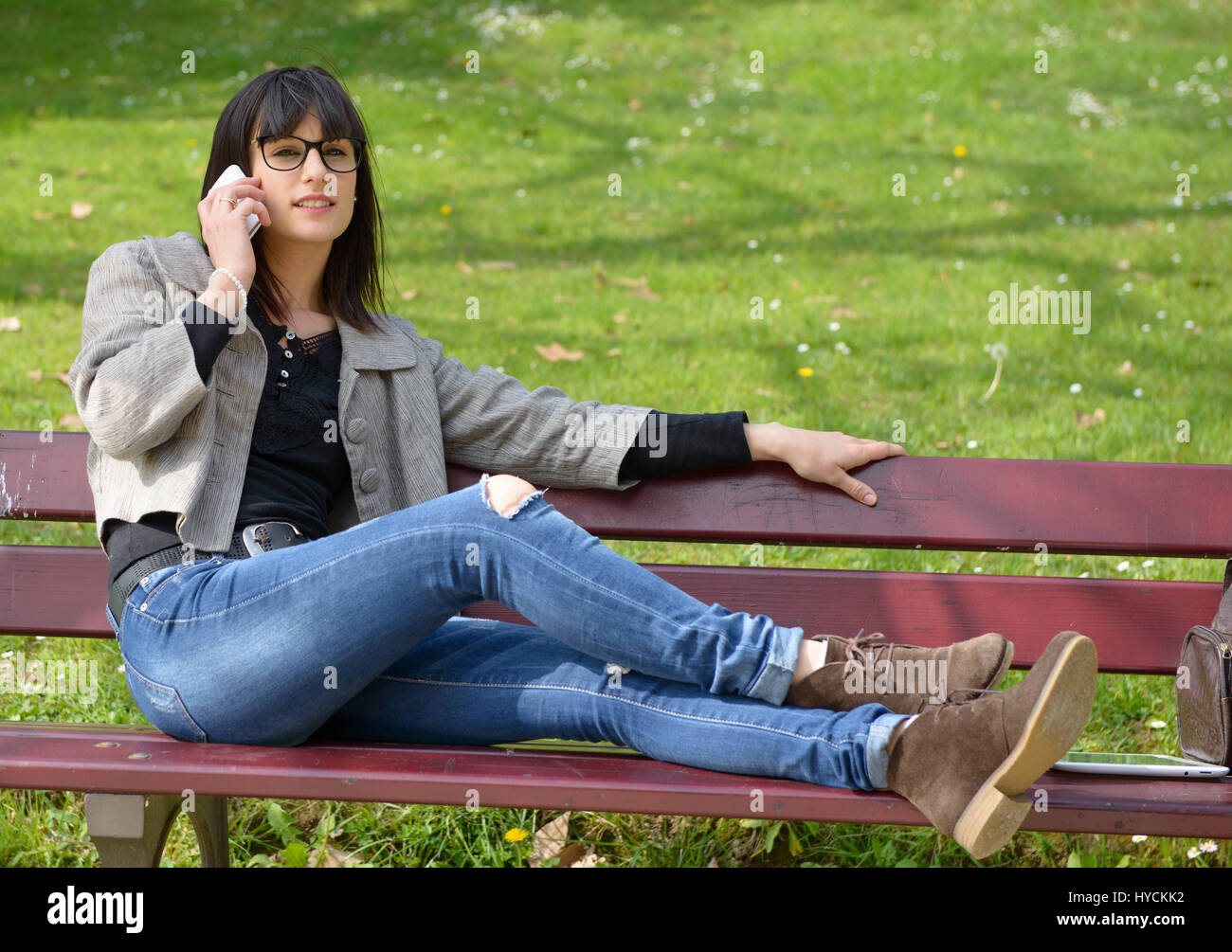 beautiful young brunette girl sitting on a bench with a mobile phone in ...