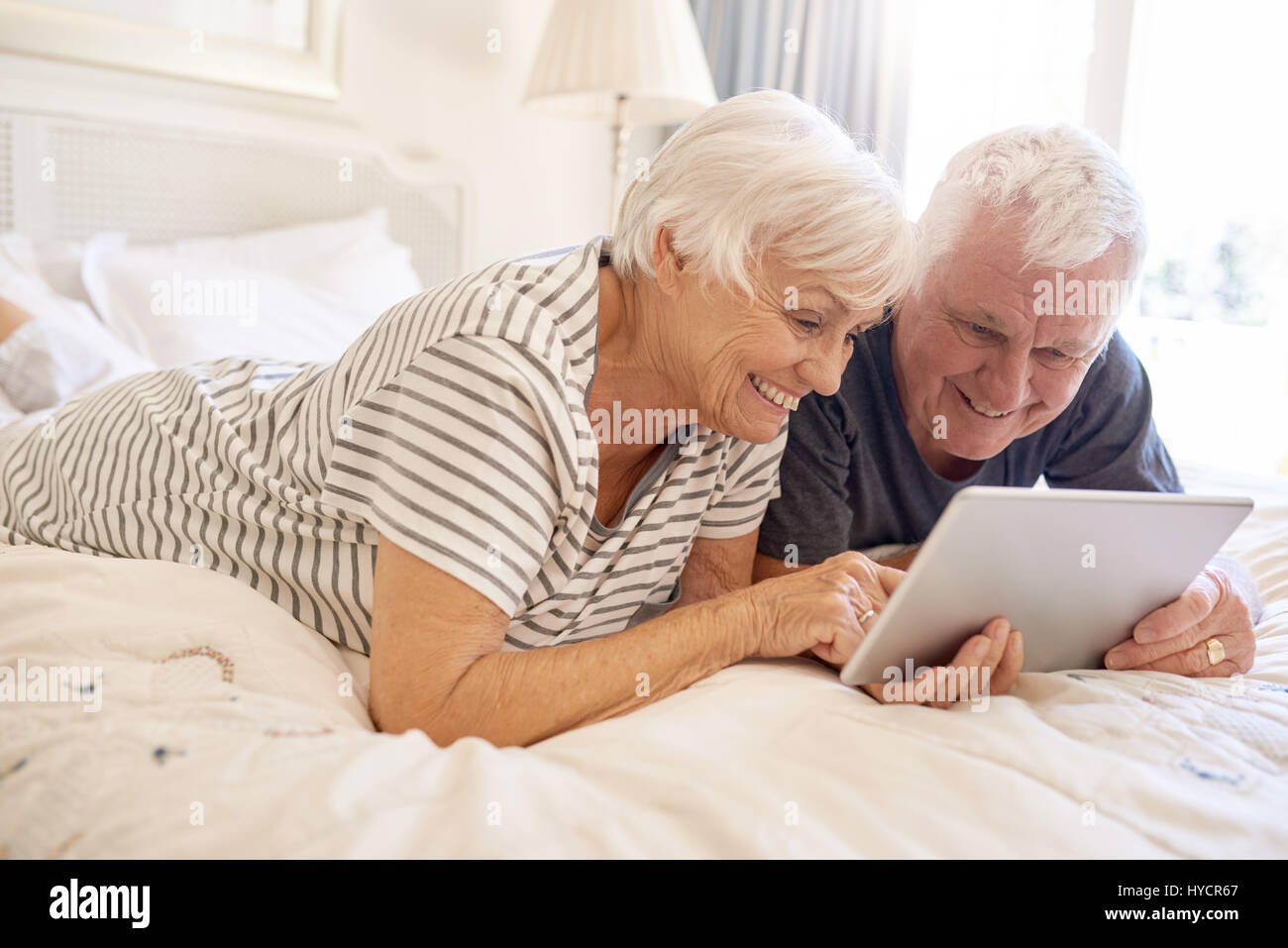 Happy senior couple lying in bed using a digital tablet Stock Photo