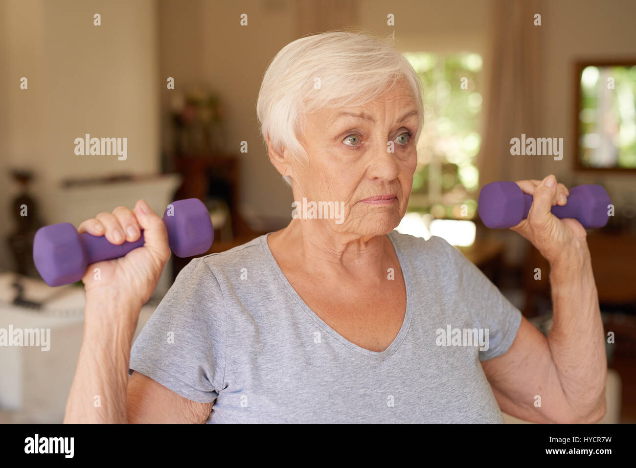 Active senior woman focused on lifting dumbells at home Stock Photo