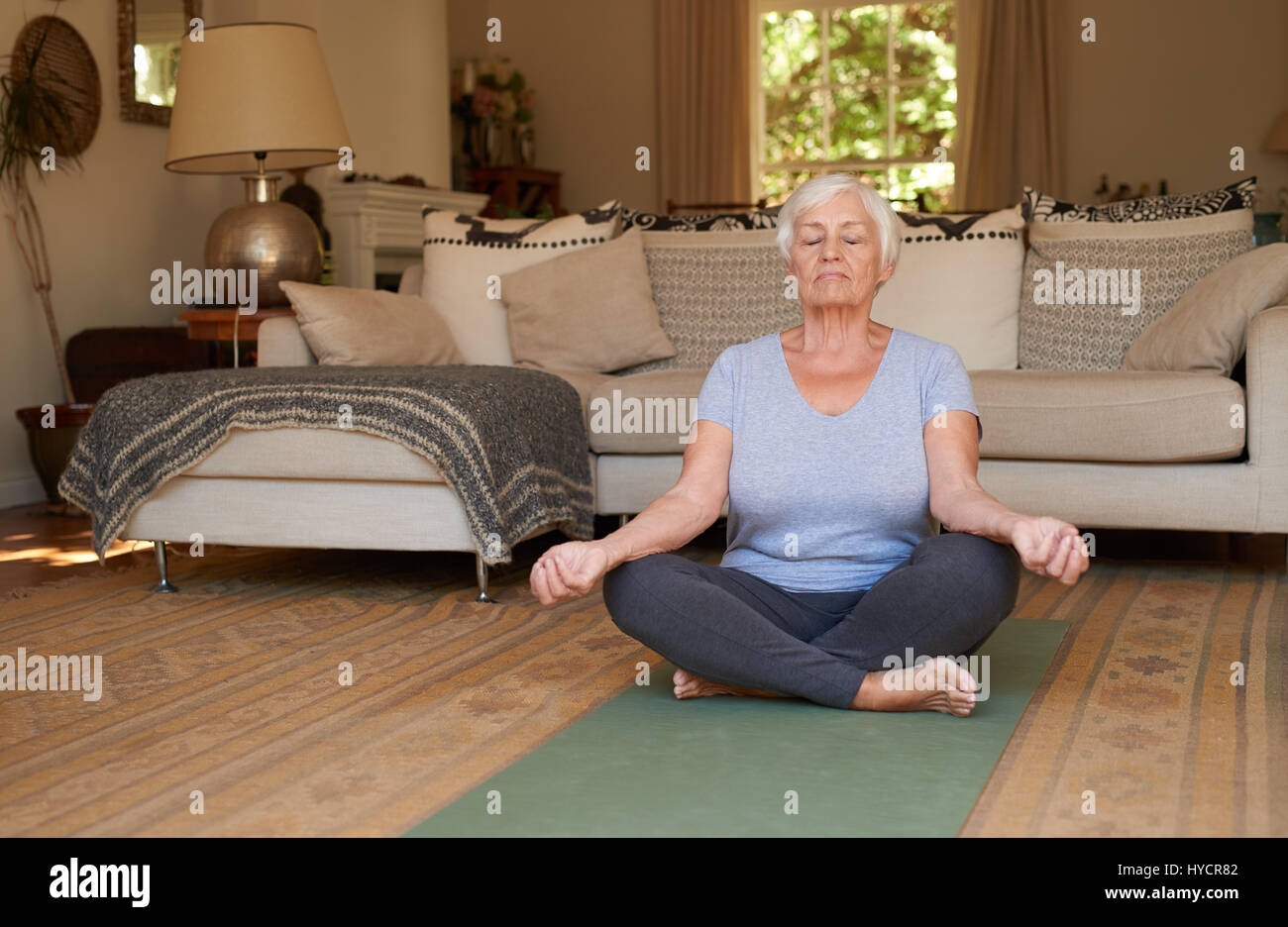 Senior woman sitting in the lotus position meditating at home Stock ...