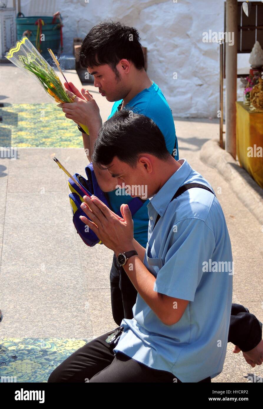 Saraburi, Thailand - January 8, 2013:  Two Thai man holding incense sticks and floral offerings pray at a Wat Phra Phutthabat outdoor shrine Stock Photo