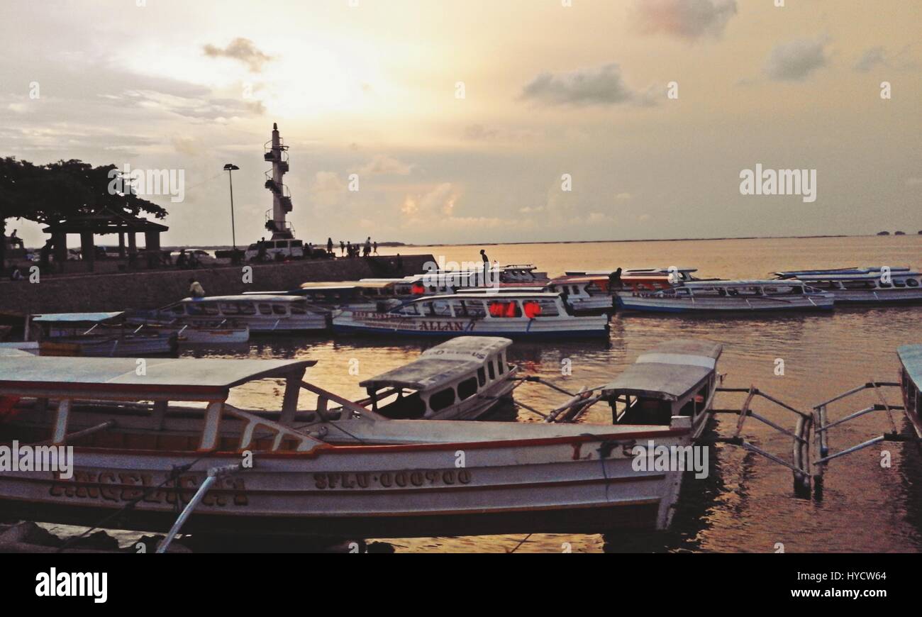 boats moored on the embankment with a lighthouse in the background Stock Photo