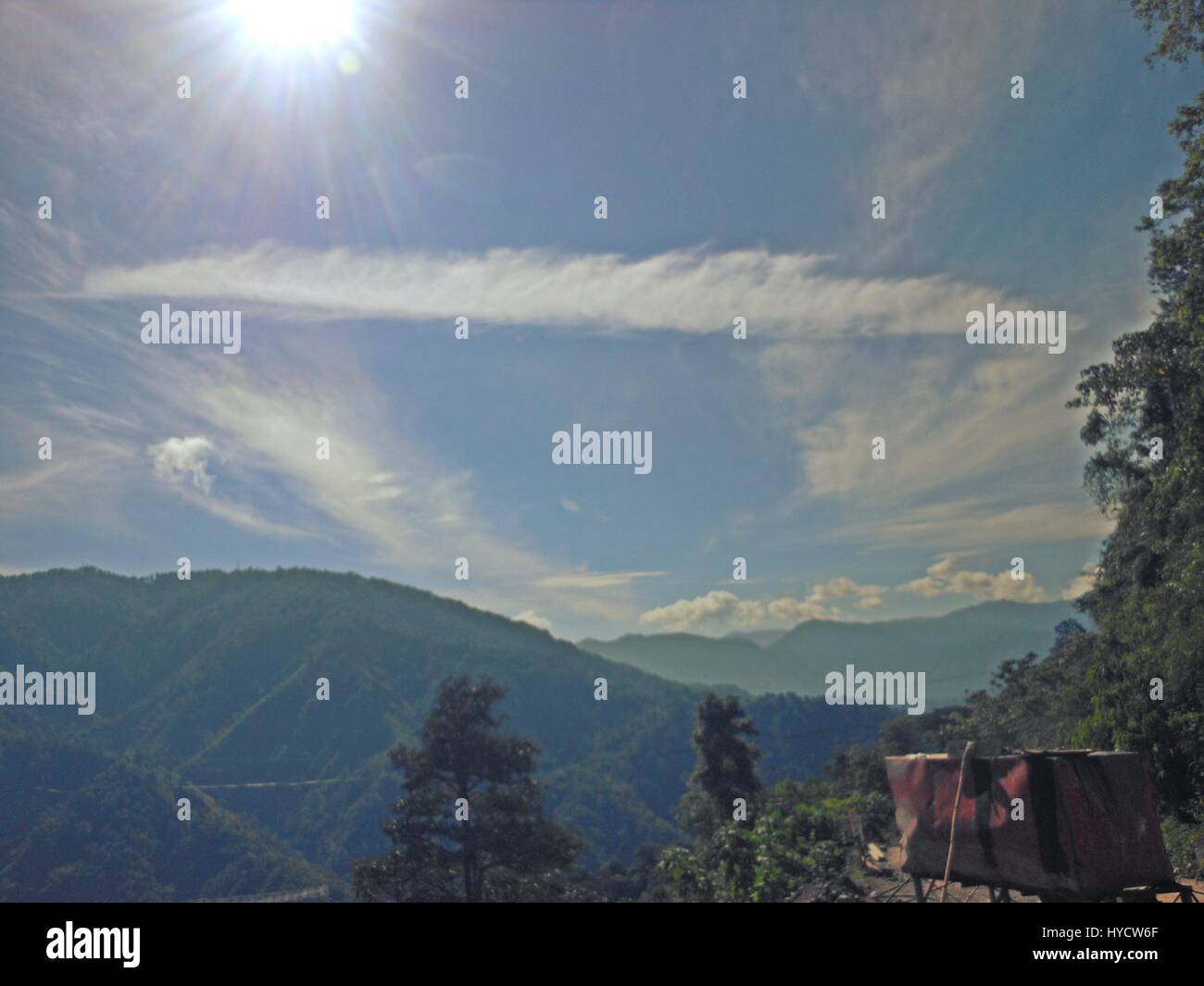 Rays of the sun in clear blue skies with beautiful cloud formations with a backdrop of mountains Stock Photo
