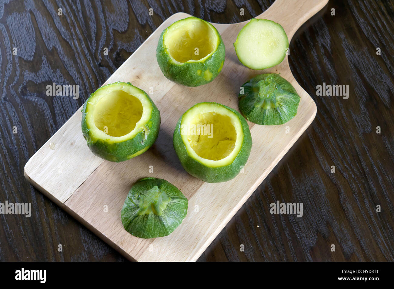 Emptied round zucchini on wooden cutting board lying on dark wooden table - Preparing stuffed zucchini recipe - Direct above Stock Photo