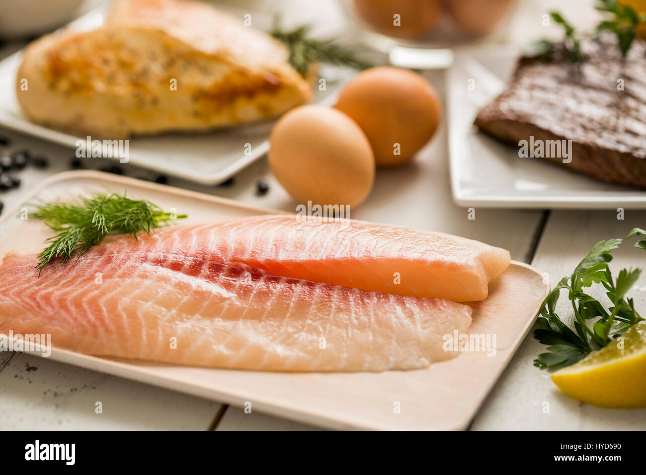 Raw tilapia fish on plate, chicken and eggs in background Stock Photo