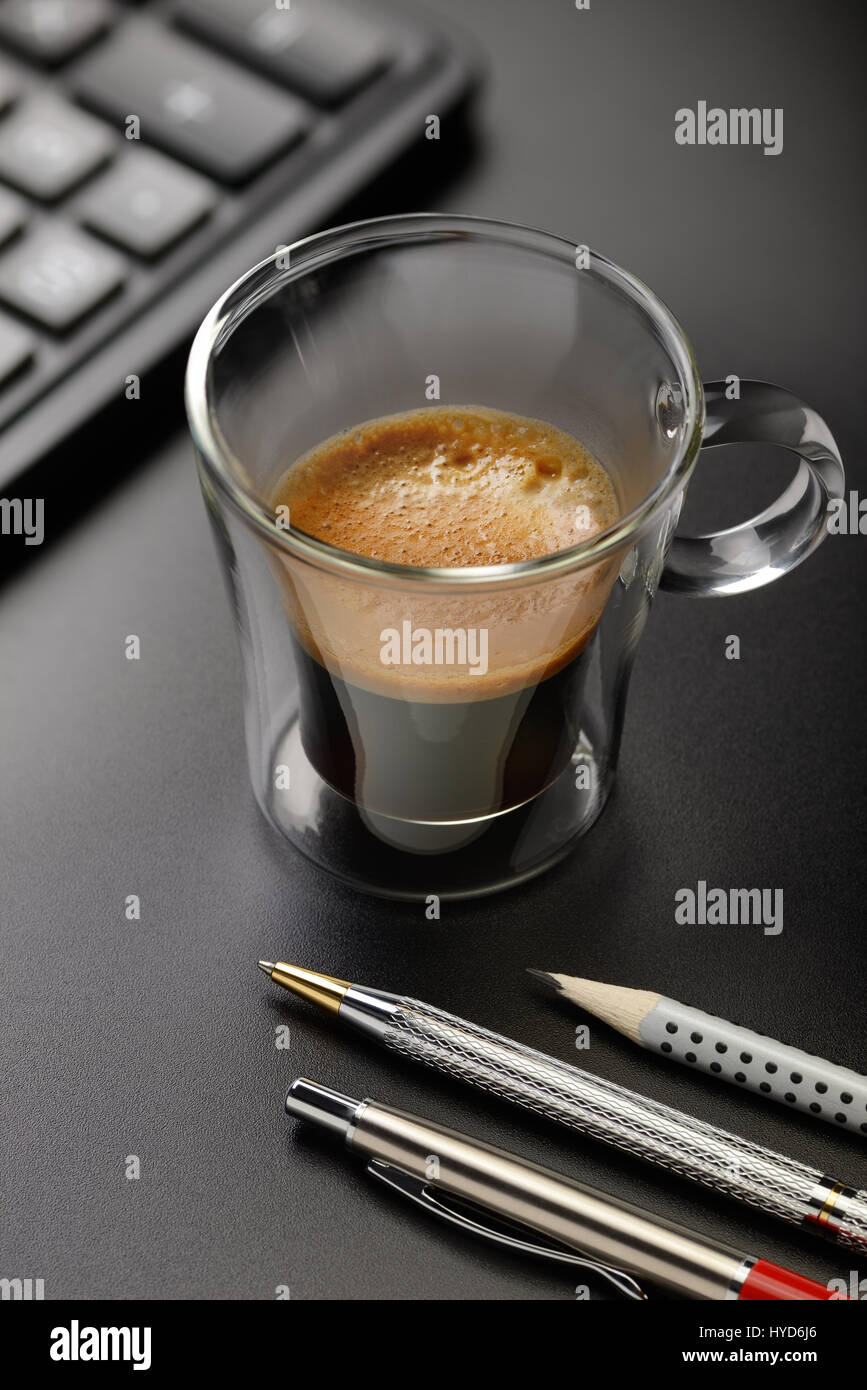 Cup of espresso coffee on the office desk with pens and calculator