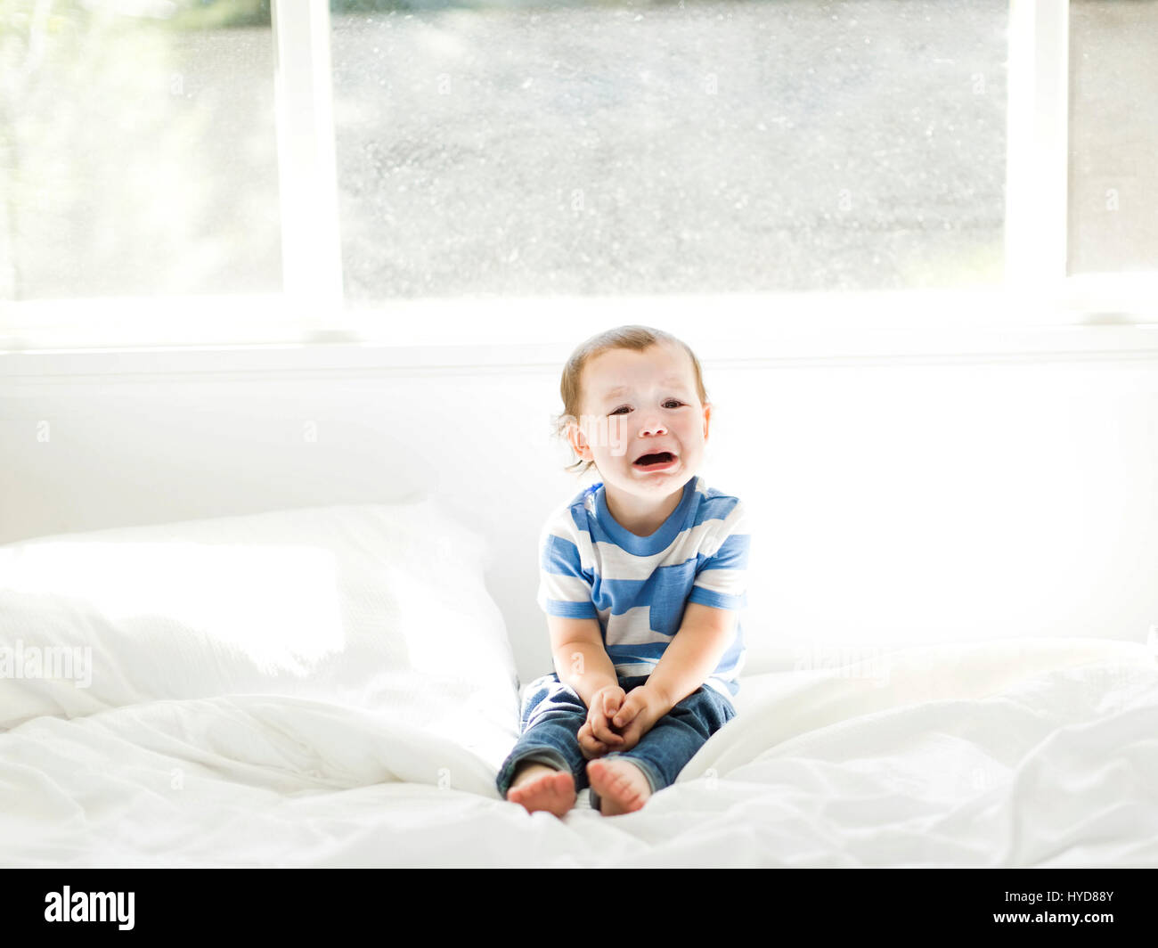 Boy (4-5) sitting on bed and crying Stock Photo