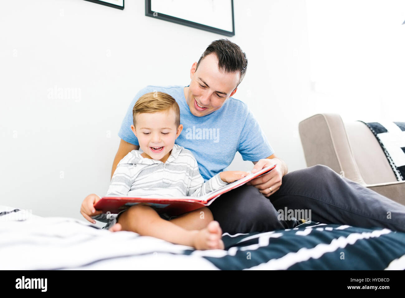 Father and son (4-5) sitting on bed and reading book Stock Photo