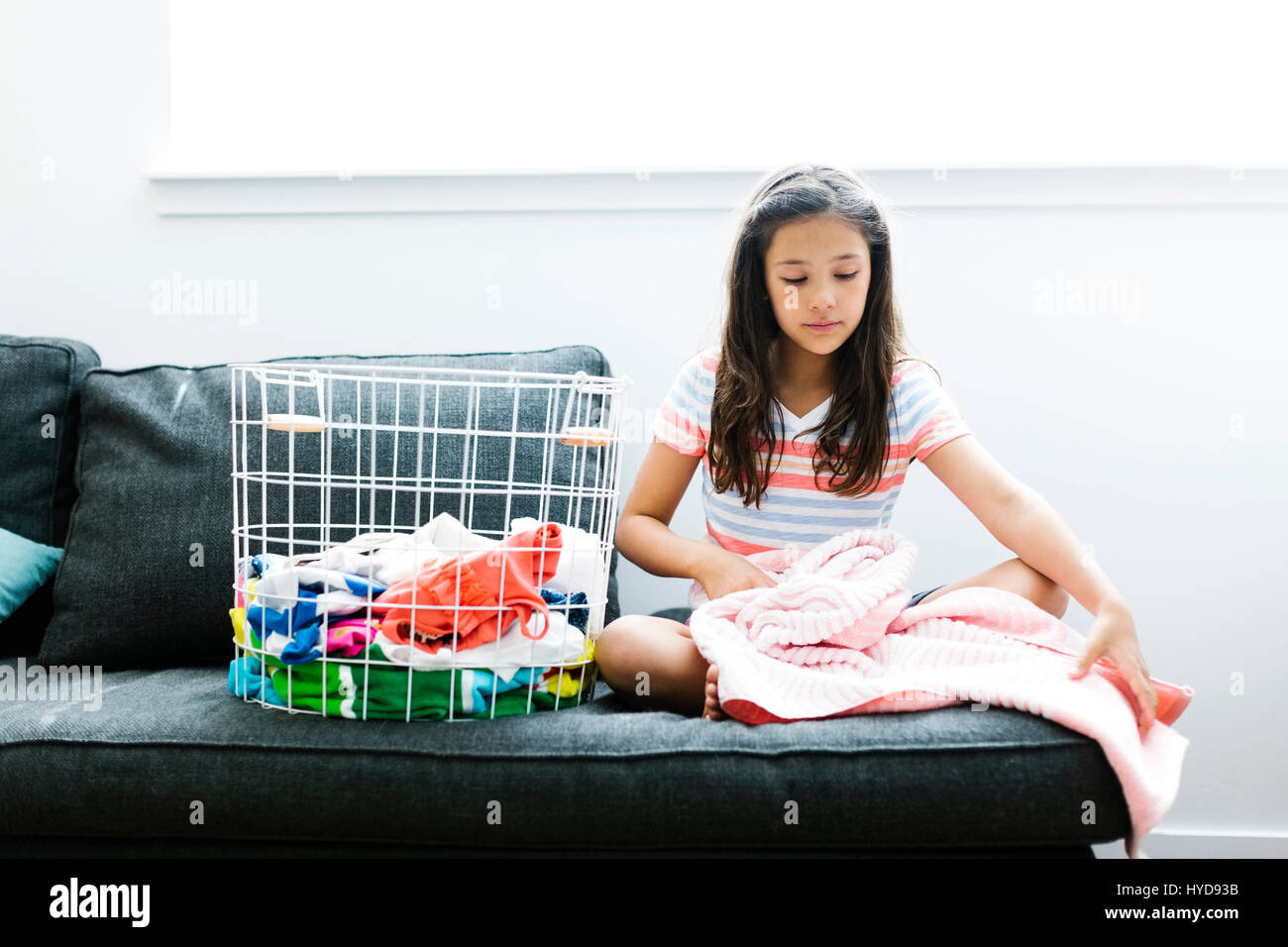 Girl (10-11 ) with laundry sitting on sofa Stock Photo