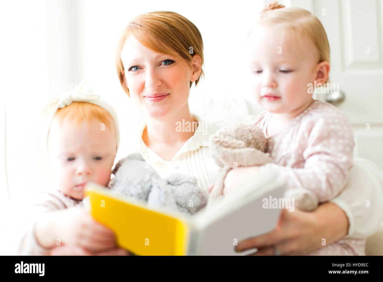 Portrait of mother reading book to daughters ( 12-17 months ) Stock Photo