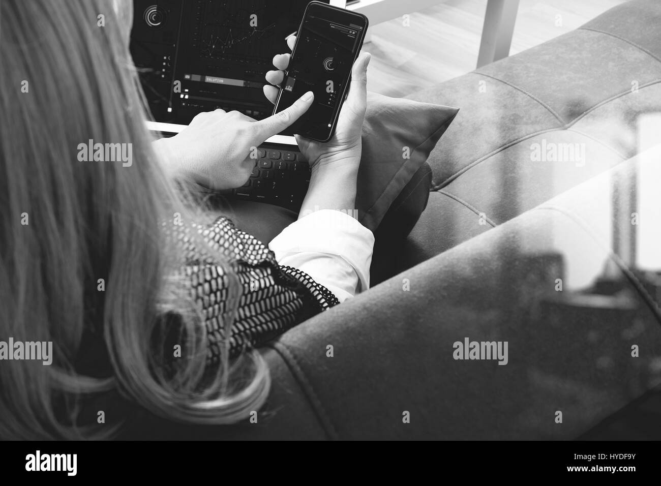 brunette woman using smart phone and digital tablet computer on sofa in living room,black and white Stock Photo