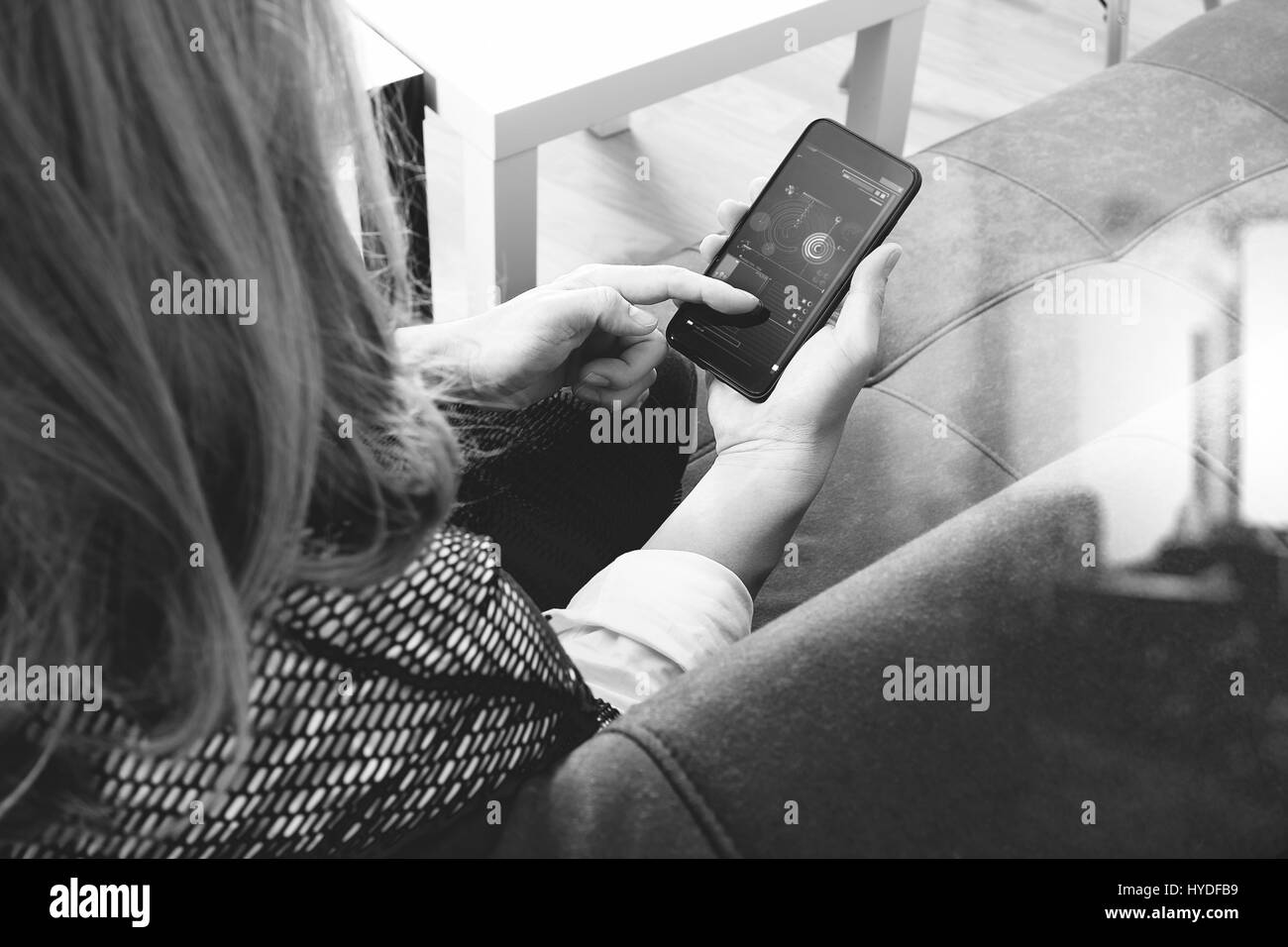 brunette woman using smart phone and digital tablet computer on sofa in living room,black and white Stock Photo