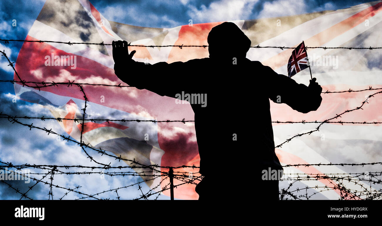 Brexit, immigration, asylum seekers... concept image. Rear view of man looking through barbed wire fence; Union Jack flag in background. Stock Photo