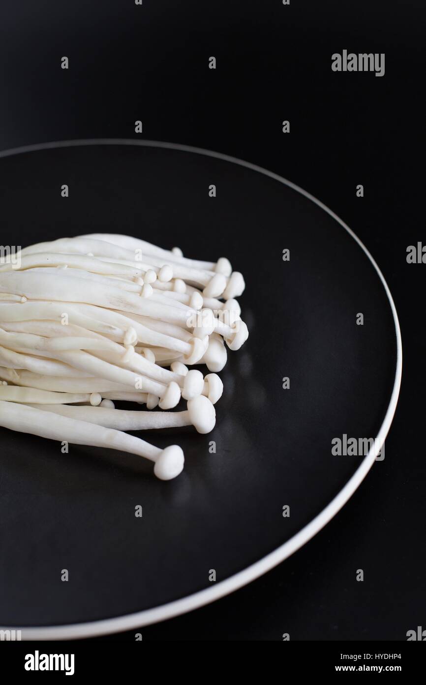 Enoki mushrooms on a black plate against a black background. Stock Photo