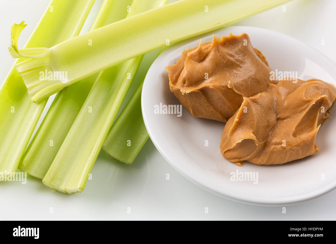 Close view of celery stalks with a bowl of peanut butter on a white plate. Stock Photo