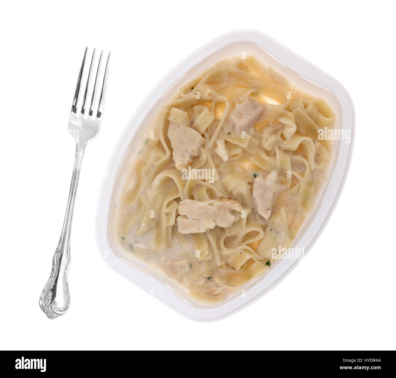 Top view of a cooked TV dinner of fettuccini with chicken and seasonings in a plastic tray plus a fork to the side isolated on a white background. Stock Photo