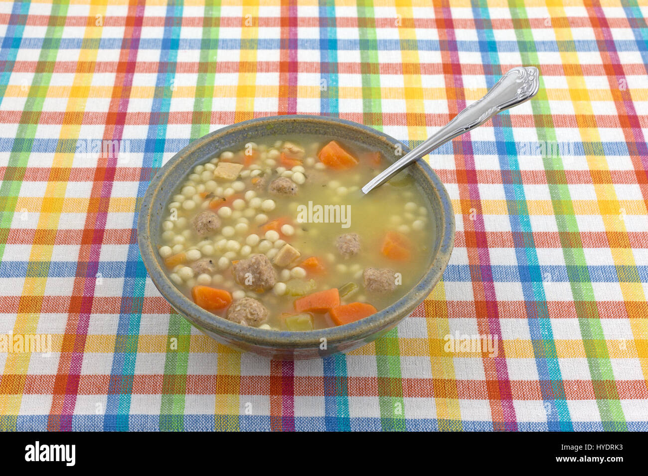 Bowl of Italian style wedding soup with a spoon in the food atop a colorful cloth place mat. Stock Photo