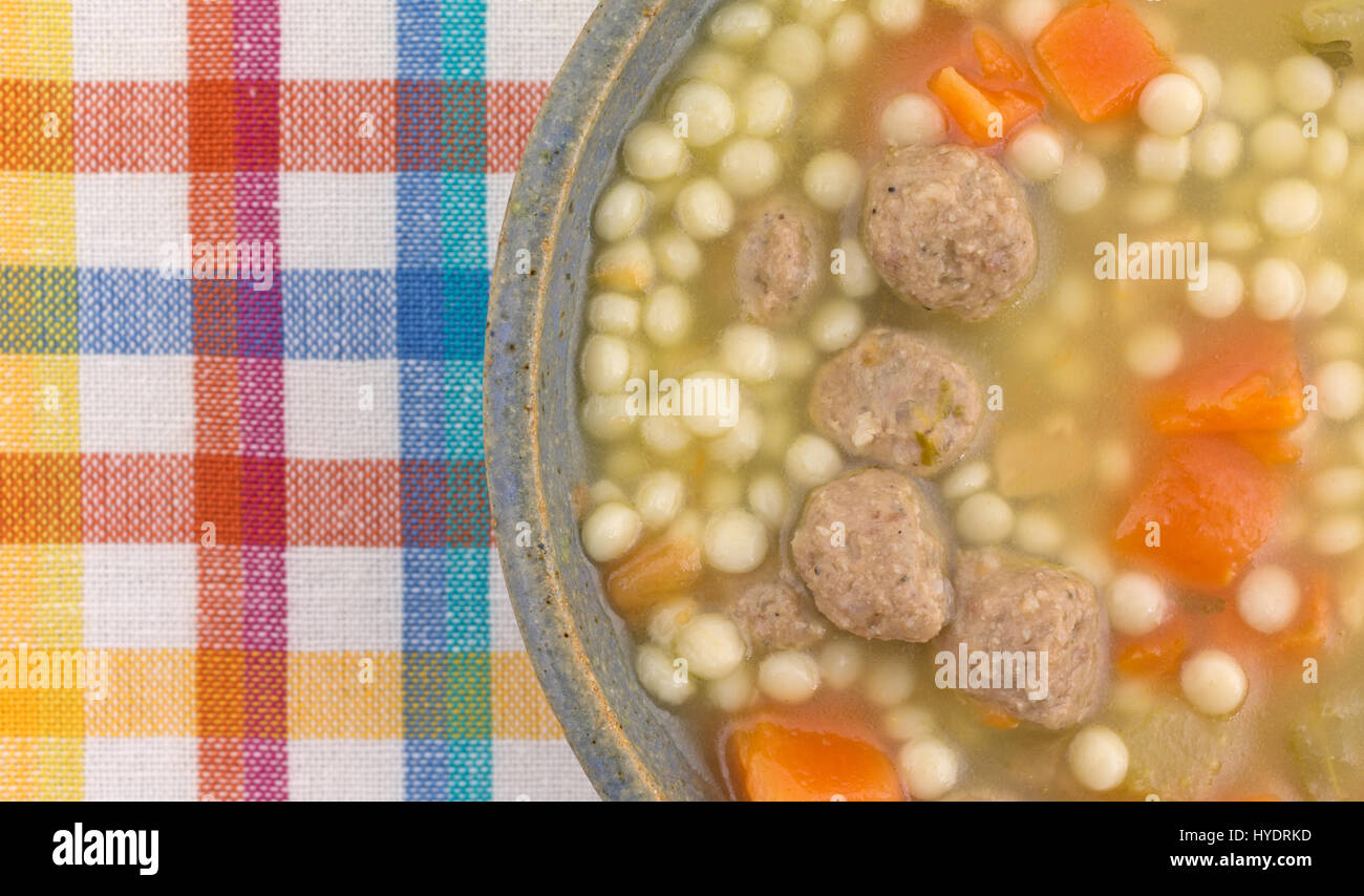Top close view of a stoneware bowl filled with Italian style wedding soup atop a colorful cloth place mat. Stock Photo