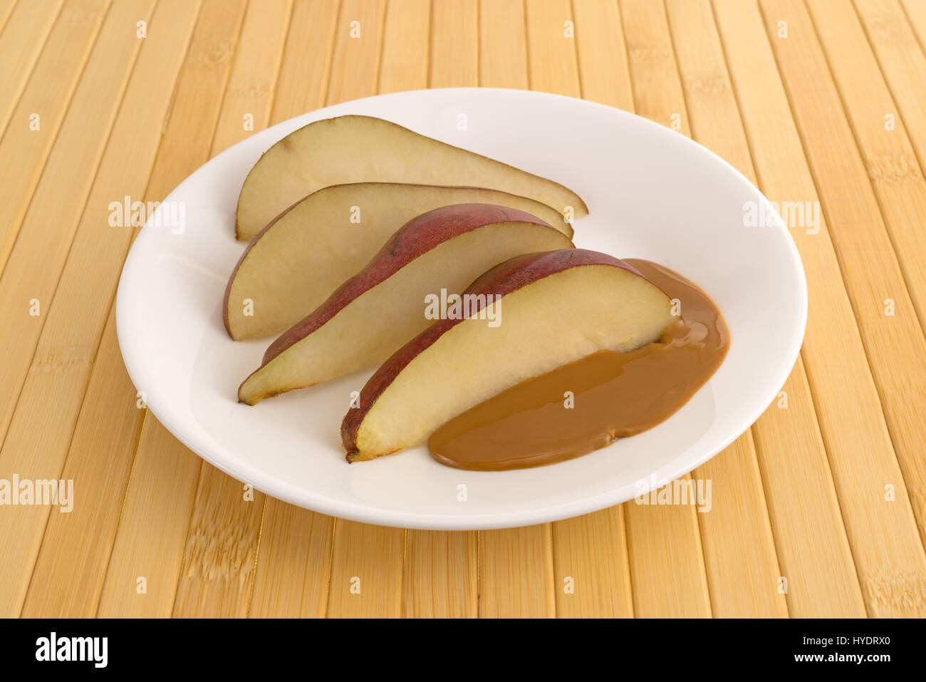 Slices of a red pear on a plate with peanut butter atop a wood plate mat. Stock Photo