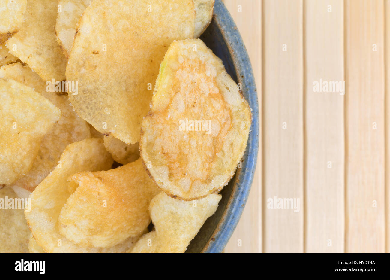 Top close view of an old stoneware bowl filled with salt and vinegar flavored potato chips on wood place mat. Stock Photo